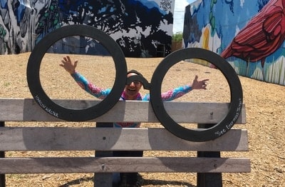 Person posing through two black circular frames on a bench with a mural backdrop — Clematis Street Bench Project