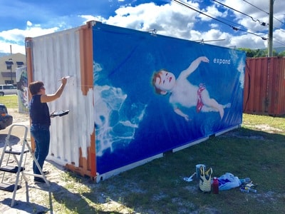 Artist painting Celestial Babies mural on shipping container